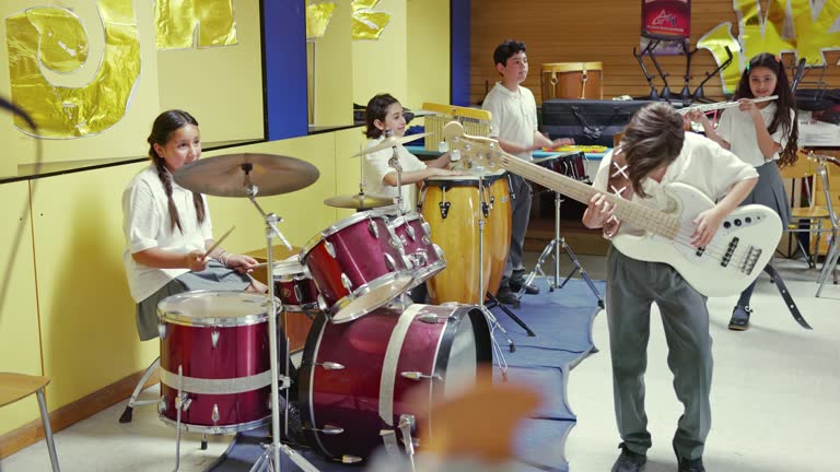 Male and female students aged 10, 11 and 14 wearing uniforms and playing electric guitar, drum set, hand drums, and flute.